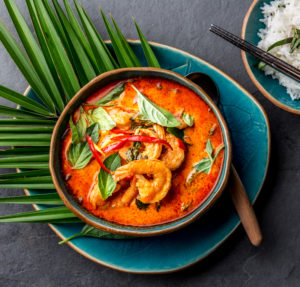 2020-02 - THAI SHRIMPS RED CURRY. Thailand Thai tradition red curry soup with shrimps prawns and coconut milk. Panaeng Curry in blue plate on gray background