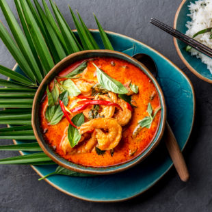 2020-02 - THAI SHRIMPS RED CURRY. Thailand Thai tradition red curry soup with shrimps prawns and coconut milk. Panaeng Curry in blue plate on gray background